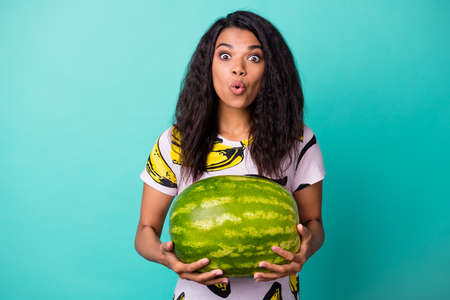 Photo of young girl hold heavy watermelon shocked expression wear banana print t-shirt isolated teal color backgroundの写真素材