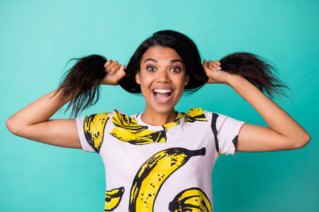 Photo of charming young girl play curly tails open mouth wear banana print t-shirt isolated turquoise color backgroundの写真素材