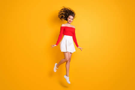 Full length body size photo jumping girl hair blowing in air smiling wearing mini skirt red top isolated on vibrant yellow color backgroundの写真素材