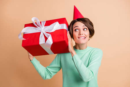 Photo of young girl shake present box wonder interested curious bite lips wear party hat isolated...