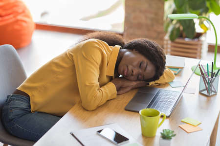 Portrait of sleepy curly brunette hair pretty girl lie on table wear yellow shirt at homeの写真素材