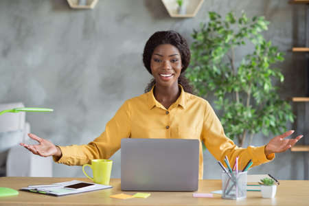 Portrait of optimistic curly brunette hair pretty girl hands up sit by table wear yellow shirt at...