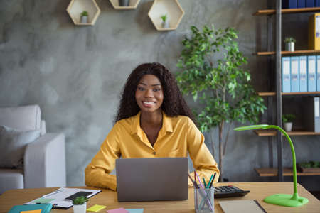 Photo of optimistic curly brunette hair nice girl write laptop sit by table wear yellow shirt at homeの写真素材
