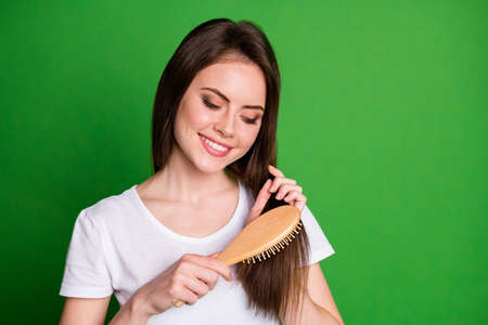 Photo portrait of focused girl brushing hair isolated on vivid green colored backgroundの写真素材
