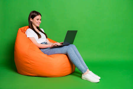 Profile photo of pretty young woman hold computer texting email freelancer dress white t-shirt jeans sneakers isolated on green backgroundの写真素材
