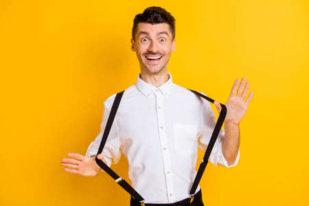 Portrait of nice attractive cheerful guy wearing white shirt pulling suspenders having fun isolated...