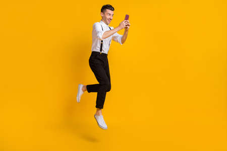 Full length body size view of nice skinny cheerful guy jumping using device browse isolated over bright yellow color backgroundの写真素材