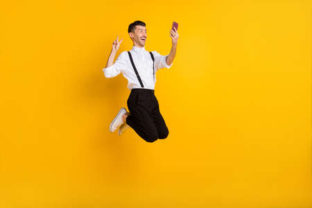 Full size profile portrait of excited handsome guy jump show v-sign make selfie isolated on yellow...