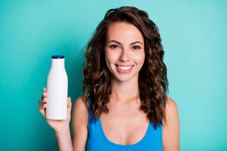 Portrait of positive wavy hair girl tourist recommend sunblock bottle best choice for exotic weekend resort wear blue beautiful swimwear isolated over teal color backgroundの写真素材