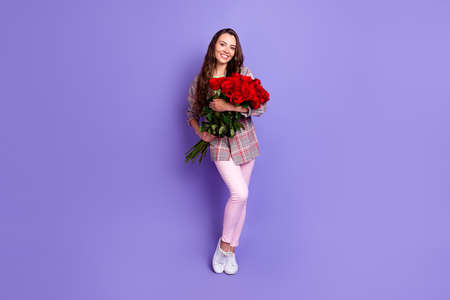 Full size photo of attractive happy nice lady hold hands flowers good mood smile isolated on purple color backgroundの写真素材