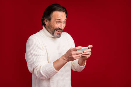 Photo of mature happy positive excited crazy smiling man playing video games on phone isolated on...