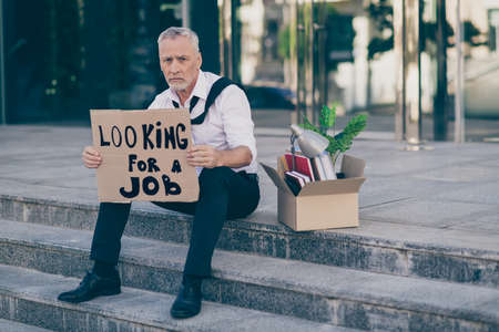 Full size photo of sad old business man sit hold banner need job wear white shirt outdoors near work centerの写真素材