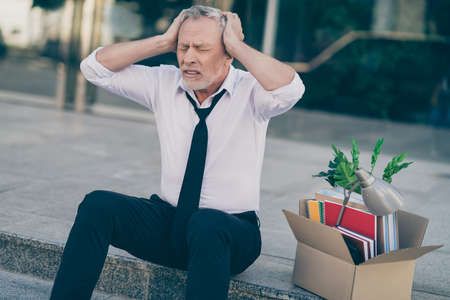 Photo of depressed hopeless elderly man hands head sit steps floor box jobless despair in outdoors...