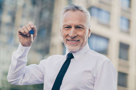 Photo of attentive good mood age businessman wear white shirt holding new apartment keys outside city streetの写真素材