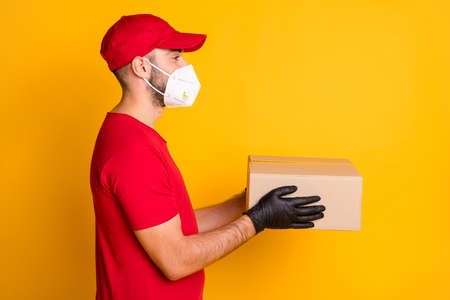 Profile side view portrait of healthy guy wearing n95 respirator bringing giving parcel shop order isolated on vivid yellow color backgroundの写真素材