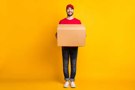 Full length body size view of nice cheerful guy mailman holding in hands bringing big parcel fast shipment isolated over vivid yellow color backgroundの写真素材