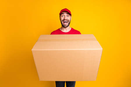 Portrait of nice cheerful guy mailman giving bringing big parcel fast shipping isolated over bright yellow color backgroundの写真素材