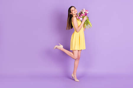 Full length body size profile side view of pretty cheerful girl holding tulips posing isolated over violet purple pastel color backgroundの写真素材