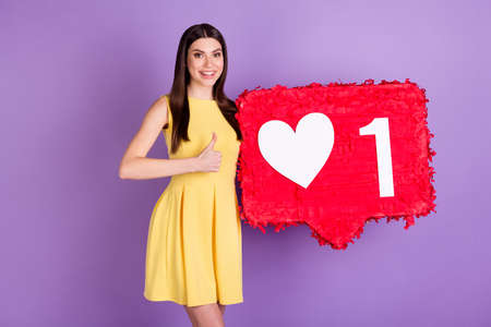 Portrait of pretty trendy cheerful girl holding in hands big like board showing thumbup isolated over violet purple pastel color backgroundの写真素材