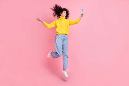 Full body photo of young latin girl happy smile jump up make selfie cellphone wear denim isolated over pastel color backgroundの写真素材