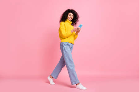 Full length photo of pretty cute wavy lady dressed yellow sweater walking chatting modern device isolated pink color backgroundの写真素材