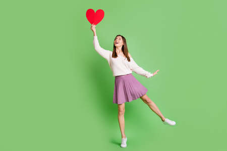 Full size photo of young beautiful happy cheerful smiling girl catch big red heart isolated on green color backgroundの写真素材