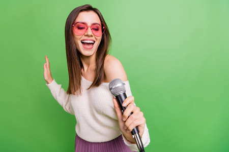 Photo of young beautiful excited smiling positive girl in funky glasses singing in microphone...