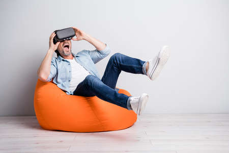 Portrait of handsome cheerful amazed mature man sitting on bean chair wear VR helmet having fun...