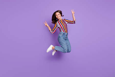 Full length body size photo of pretty girl jumping up showing v-sign gesture smiling isolated on vivid purple color backgroundの写真素材