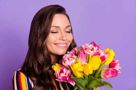 Photo portrait of happy woman smelling aroma of tulips flowers bunch smiling isolated vibrant violet color backgroundの写真素材