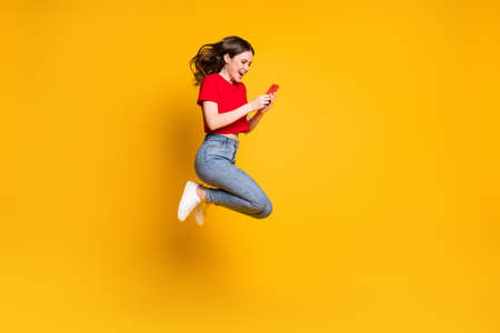 Full body photo of cheerful girl jump use smartphone discounts isolated over bright shine color backgroundの写真素材
