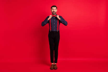Full size photo of young happy excited cheerful handsome gentleman adjust bow tie isolated on red color backgroundの写真素材