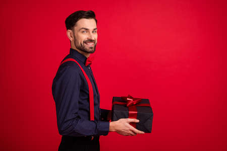 Profile side photo of young handsome cheerful smiling gentleman give present in copyspace isolated on red color backgroundの写真素材