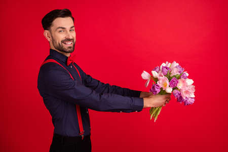 Photo of young cheerful gentleman give bouquet in copyspace boyfriend on date isolated on red color backgroundの写真素材