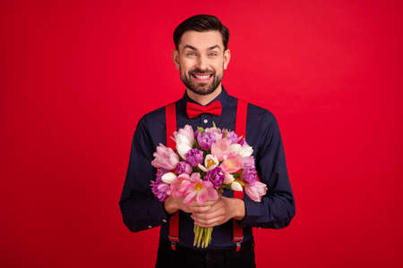 Photo of young happy cheerful handsome gentleman hold bouquet celebrate woman day isolated on red color backgroundの写真素材