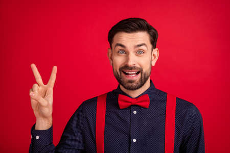 Photo of young handsome positive cheerful excited gentleman showing v-sign greetings isolated on red color backgroundの写真素材