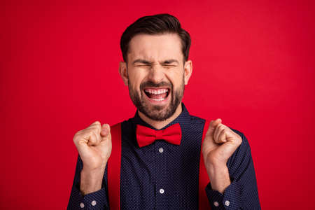 Portrait of young happy excited smiling crazy screaming man hold fist in victory triumph isolated on red color backgroundの写真素材