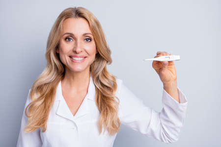 Photo of mature happy positive cheerful smiling woman nurse measure temperature isolated on grey color backgroundの写真素材