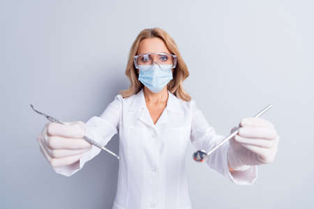 Photo of mature stomatologist woman in face mask doing dental procedure in camera isolated on grey...