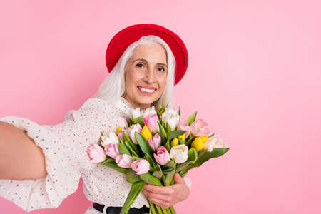 Self-portrait of attractive cheerful grey-haired retired pensioner elderly granny holding fresh...