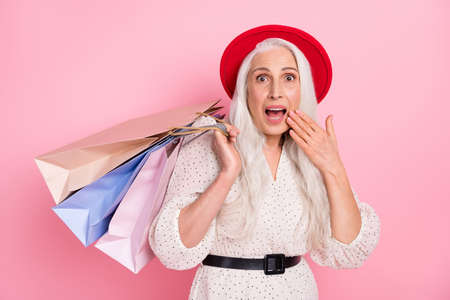 Portrait of attractive amazed cheerful grey-haired woman carrying new things clothes isolated over pink pastel color backgroundの写真素材