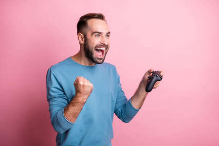 Photo of excited lucky guy wear blue pullover playing games looking empty space rising fist isolated...