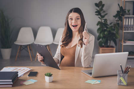Photo portrait of excited pregnant woman having idea writing holding pen clipboard at desk in modern...