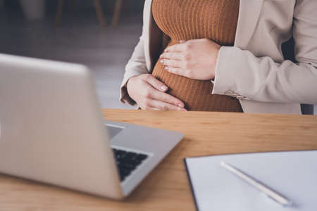 Cropped photo of business lady sit desk hands embrace big belly wear jacket workplace office indoors