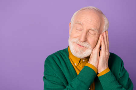 Portrait of satisfied aged man closed eyes folded arms palms under cheek isolated on purple color...