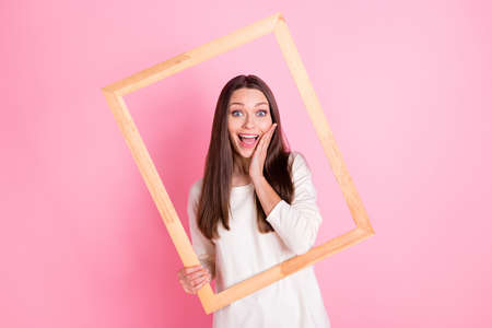 Photo of charming excited young lady wear white shirt arm cheek hlding wooden frame isolated pink color backgroundの写真素材