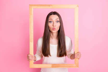 Photo of cute charming young woman wear white clothes sending kiss big wooden photo frame isolated pink color backgroundの写真素材