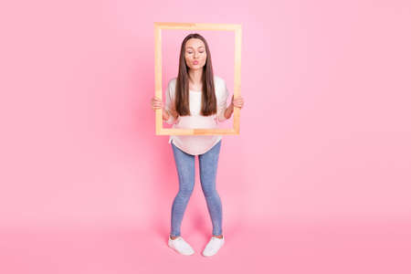 Photo of adorable funny young woman wear white clothes sending kiss wooden frame isolated pink color backgroundの写真素材