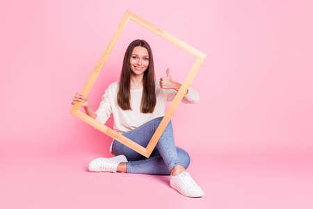 Full size photo of pretty positive person sit on floor hold frame shot thumb up isolated on pink...