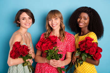 Photo of young three cheerful girls happy positive smile hold flowers bouquet woman day spring isolated over blue color backgroundの写真素材